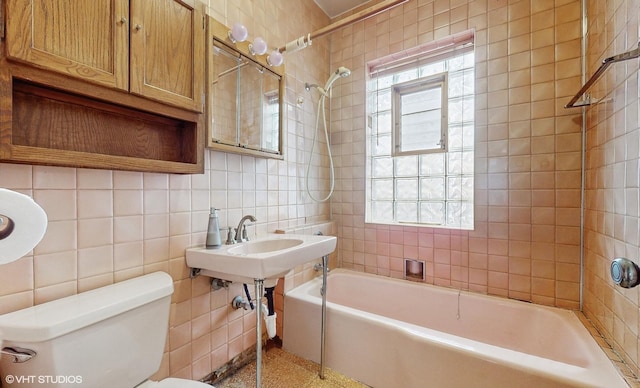 bathroom featuring tiled shower / bath combo, toilet, and tile walls