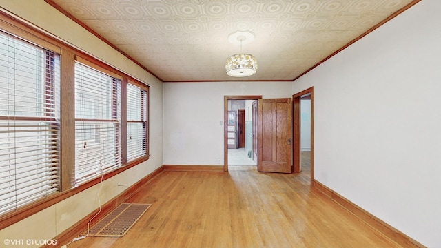 empty room with light wood-type flooring, crown molding, and a notable chandelier