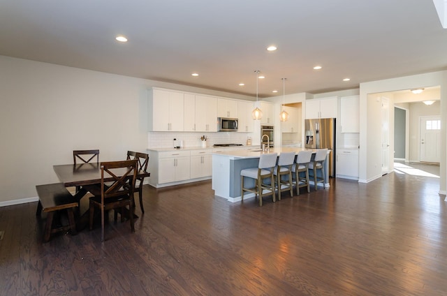 kitchen with dark wood-type flooring, a center island with sink, a kitchen breakfast bar, appliances with stainless steel finishes, and decorative backsplash