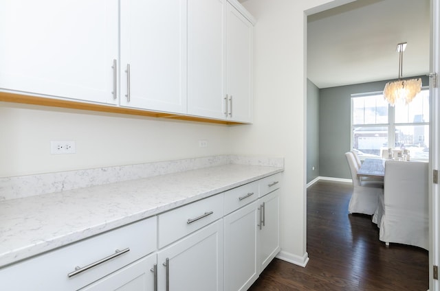 kitchen with light stone counters, baseboards, dark wood-style flooring, white cabinets, and a notable chandelier