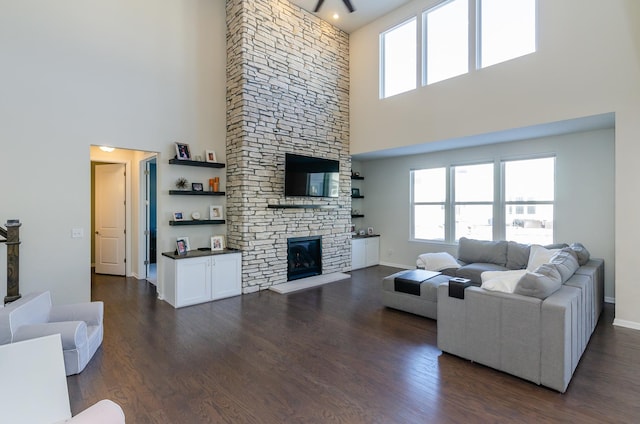 living room featuring dark wood-style floors, a stone fireplace, a healthy amount of sunlight, and baseboards