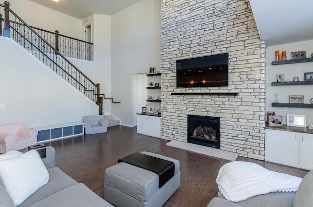 living area featuring stairs, a stone fireplace, a towering ceiling, and dark wood-style flooring