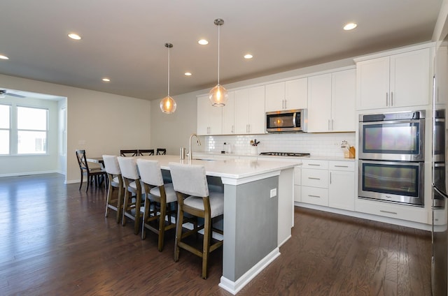 kitchen with dark wood-type flooring, a kitchen island with sink, a sink, tasteful backsplash, and stainless steel appliances