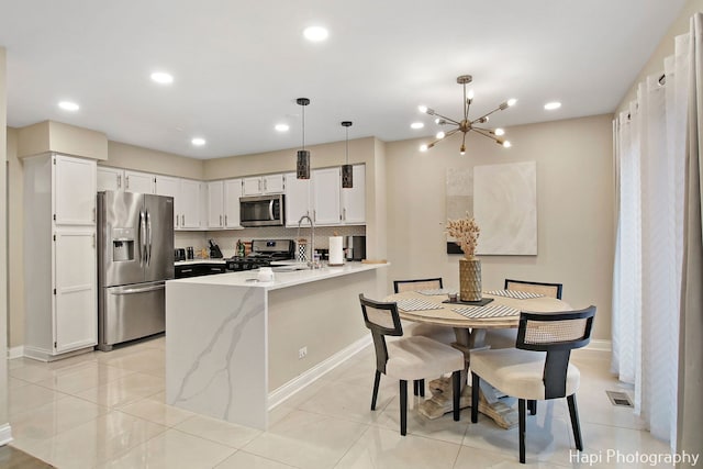 kitchen with kitchen peninsula, light tile patterned floors, appliances with stainless steel finishes, decorative light fixtures, and white cabinetry