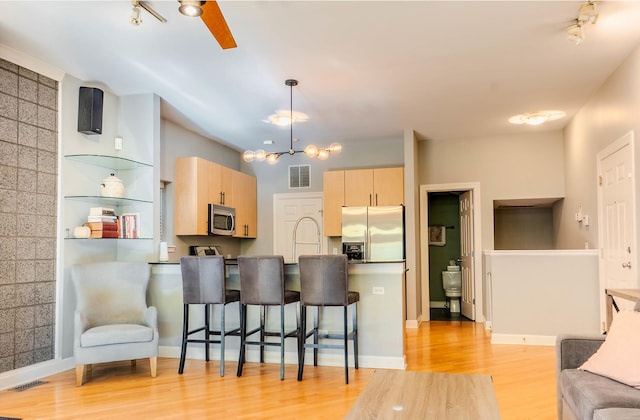 kitchen featuring appliances with stainless steel finishes, light wood-type flooring, a kitchen breakfast bar, light brown cabinetry, and hanging light fixtures