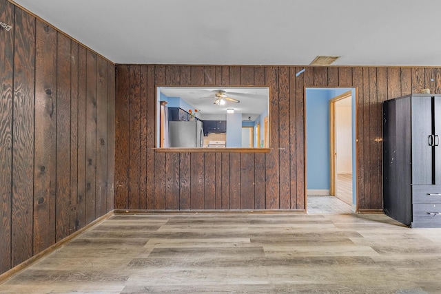 unfurnished room featuring ceiling fan, light hardwood / wood-style floors, and wooden walls