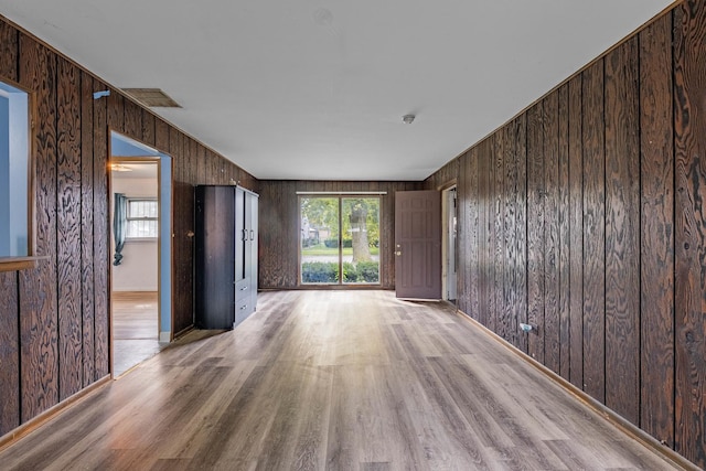 unfurnished room featuring light hardwood / wood-style flooring, a healthy amount of sunlight, and wood walls