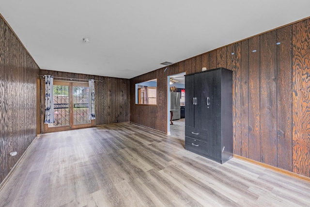 unfurnished living room featuring ceiling fan, wood walls, and light wood-type flooring