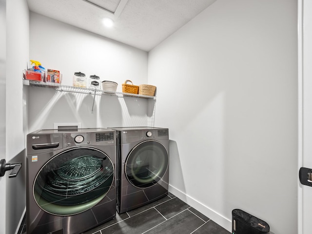 laundry room featuring washing machine and clothes dryer, a textured ceiling, and dark tile patterned flooring