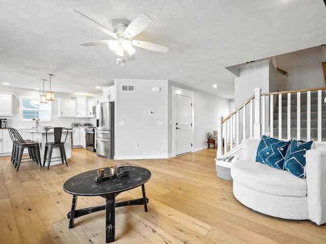 living room featuring ceiling fan, sink, a textured ceiling, and light wood-type flooring