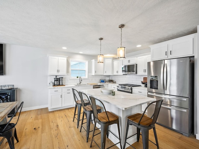 kitchen with appliances with stainless steel finishes, sink, a center island, white cabinetry, and hanging light fixtures