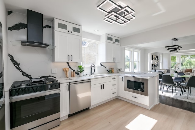 kitchen with stainless steel appliances, white cabinetry, wall chimney exhaust hood, and sink