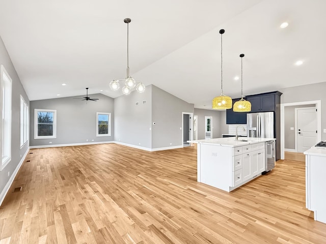 kitchen featuring stainless steel fridge, ceiling fan with notable chandelier, sink, hanging light fixtures, and lofted ceiling