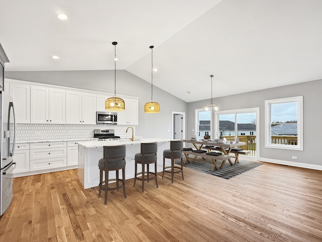 kitchen featuring appliances with stainless steel finishes, tasteful backsplash, a center island with sink, white cabinets, and hanging light fixtures