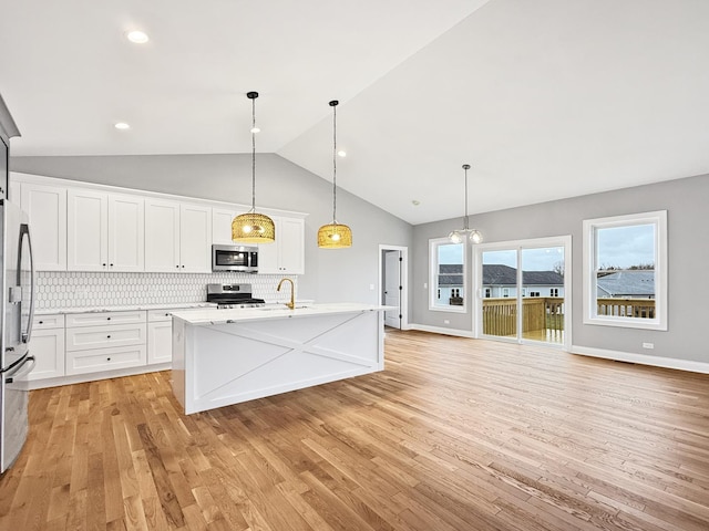 kitchen featuring tasteful backsplash, an island with sink, decorative light fixtures, white cabinets, and appliances with stainless steel finishes