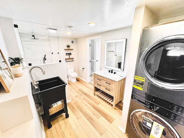 clothes washing area with sink, stacked washer and dryer, and light wood-type flooring