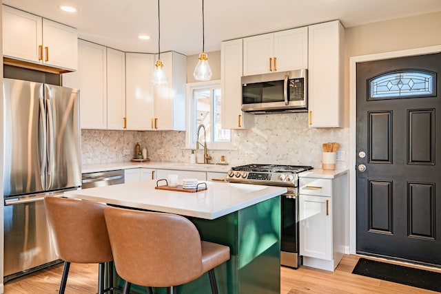 kitchen with appliances with stainless steel finishes, a kitchen island, sink, white cabinetry, and hanging light fixtures