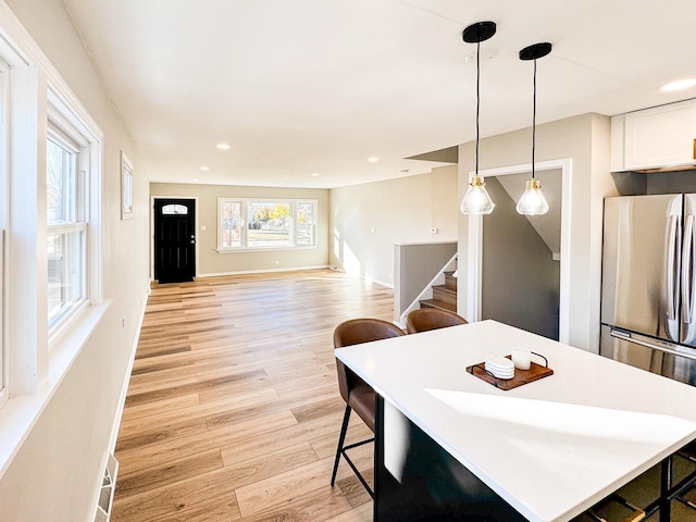 kitchen featuring light wood-type flooring, decorative light fixtures, white cabinets, stainless steel refrigerator, and a breakfast bar area