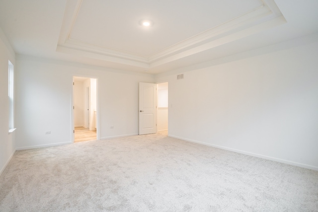 unfurnished bedroom featuring ensuite bathroom, a raised ceiling, light colored carpet, and crown molding