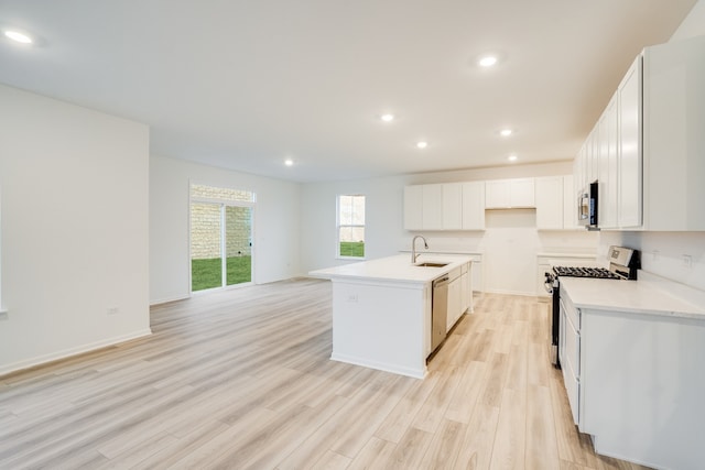 kitchen featuring stainless steel appliances, sink, a center island with sink, white cabinets, and light hardwood / wood-style floors