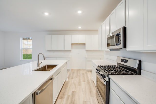 kitchen with sink, light stone countertops, appliances with stainless steel finishes, light hardwood / wood-style floors, and white cabinetry