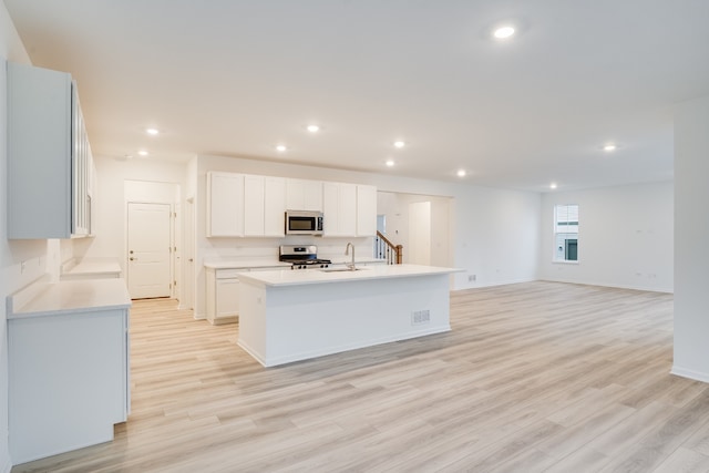 kitchen featuring a center island with sink, sink, appliances with stainless steel finishes, light hardwood / wood-style floors, and white cabinetry