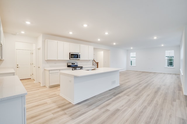 kitchen with white cabinets, appliances with stainless steel finishes, a center island with sink, and light hardwood / wood-style flooring