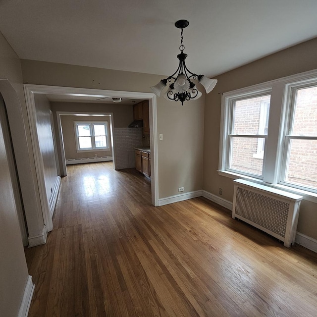 unfurnished dining area with radiator, a healthy amount of sunlight, a baseboard heating unit, an inviting chandelier, and light hardwood / wood-style floors