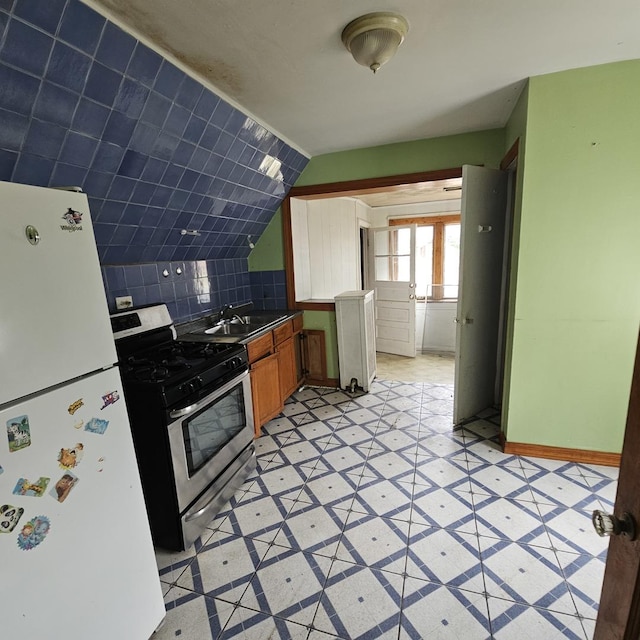 kitchen featuring sink, tasteful backsplash, white refrigerator, lofted ceiling, and stainless steel range with gas stovetop