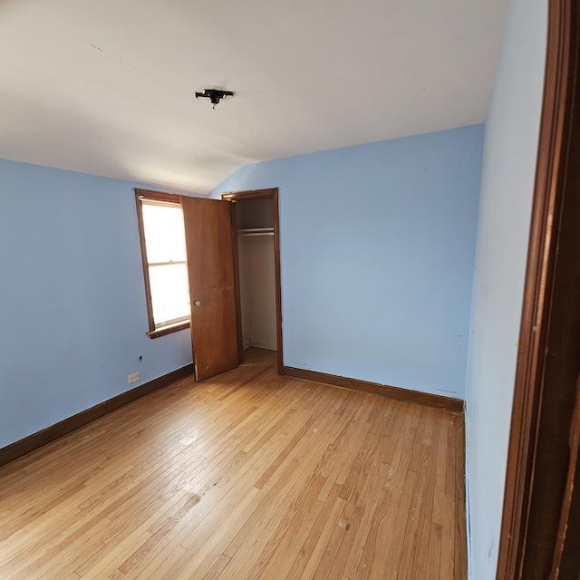 unfurnished bedroom with a closet, vaulted ceiling, and light wood-type flooring