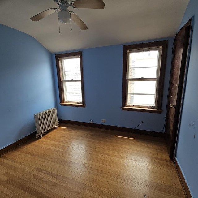 unfurnished room with lofted ceiling, light wood-type flooring, radiator heating unit, and a wealth of natural light