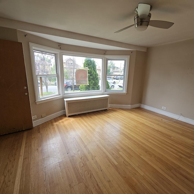 empty room featuring ceiling fan, radiator heating unit, and light wood-type flooring