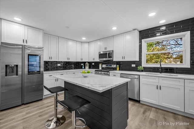 kitchen featuring white cabinetry, sink, stainless steel appliances, light stone counters, and a kitchen island