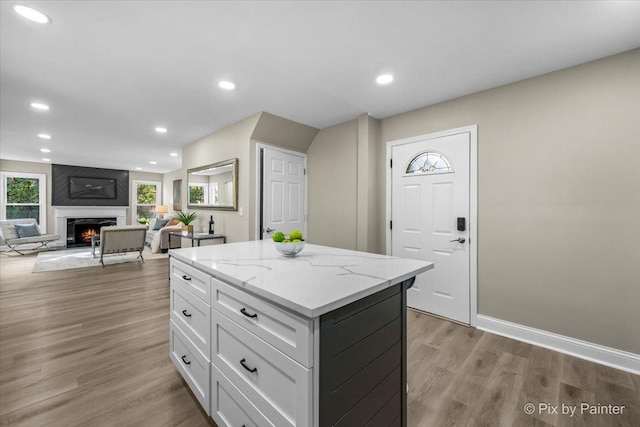 kitchen featuring light stone counters, a large fireplace, white cabinets, a center island, and light hardwood / wood-style floors