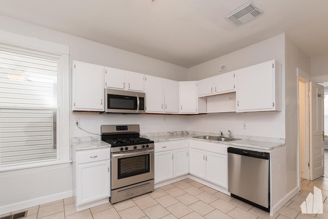 kitchen with white cabinets, sink, light tile patterned flooring, light stone counters, and stainless steel appliances