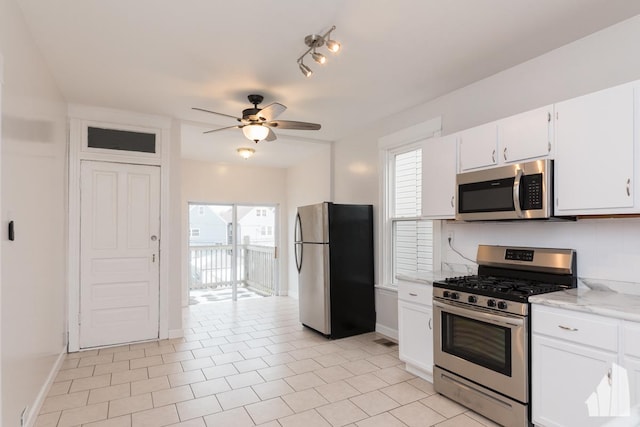 kitchen featuring ceiling fan, appliances with stainless steel finishes, light tile patterned flooring, light stone counters, and white cabinetry