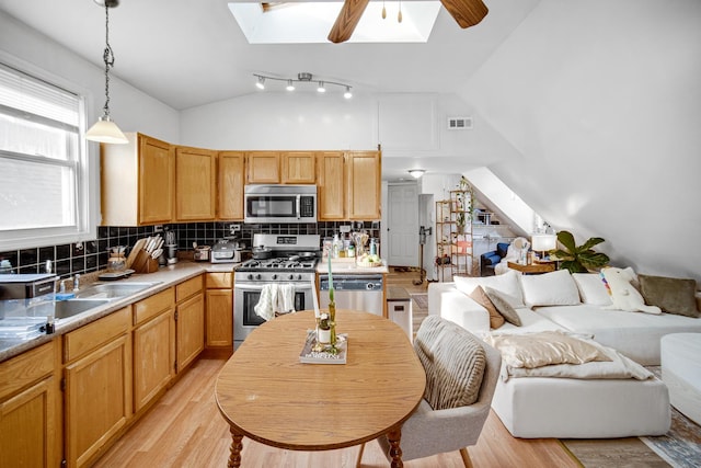 kitchen with decorative backsplash, appliances with stainless steel finishes, vaulted ceiling with skylight, ceiling fan, and hanging light fixtures