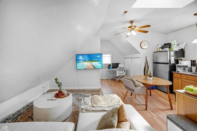 living room featuring vaulted ceiling with skylight, ceiling fan, and light hardwood / wood-style floors