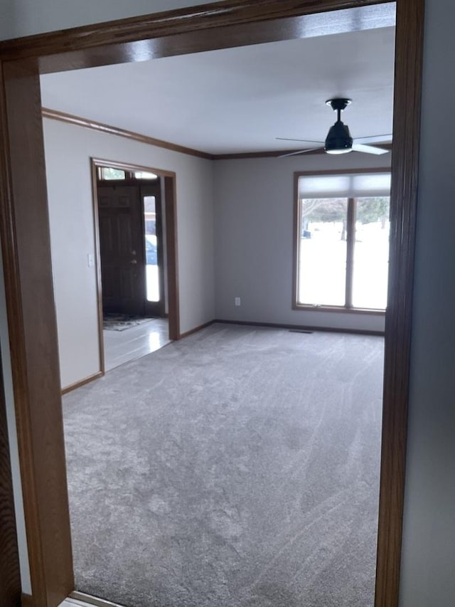 carpeted spare room featuring ceiling fan, crown molding, and a healthy amount of sunlight