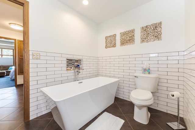 bathroom featuring toilet, tile patterned floors, tile walls, and a bathing tub