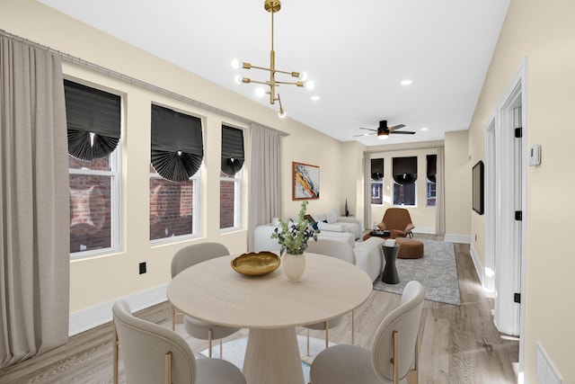 dining space featuring ceiling fan with notable chandelier and light hardwood / wood-style flooring