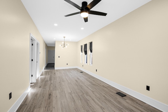 unfurnished room featuring ceiling fan with notable chandelier and light wood-type flooring