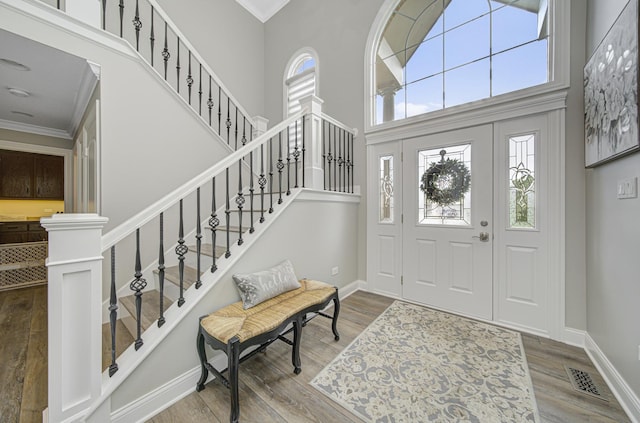 entryway with crown molding, a towering ceiling, and wood-type flooring