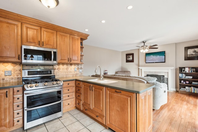 kitchen with sink, stainless steel appliances, a fireplace, decorative backsplash, and kitchen peninsula