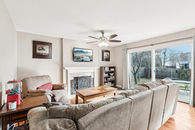 living room featuring ceiling fan, a tiled fireplace, and light hardwood / wood-style flooring