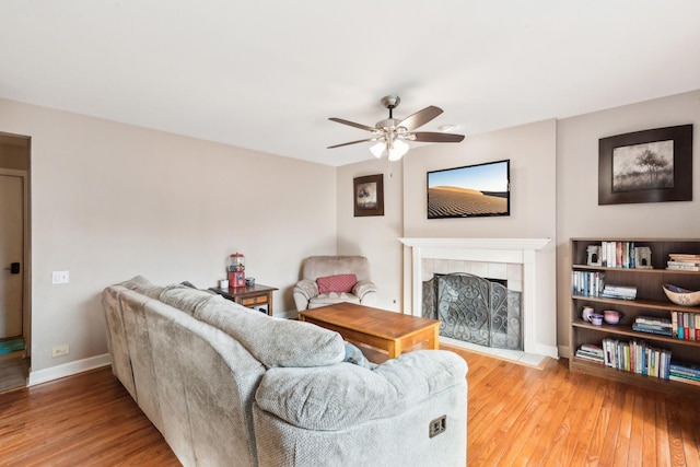 living room with a fireplace, ceiling fan, and light wood-type flooring