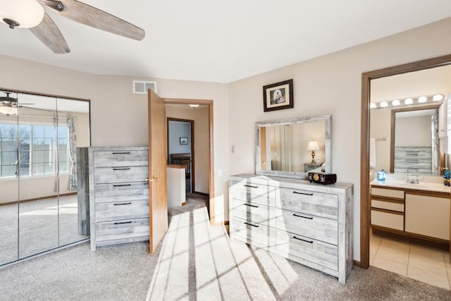 bedroom with ceiling fan, light colored carpet, ensuite bathroom, and sink