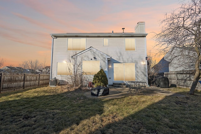 back house at dusk featuring cooling unit and a lawn