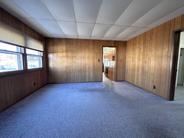 empty room featuring a drop ceiling, wood walls, and light carpet