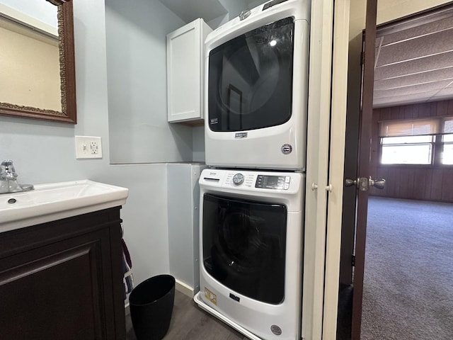 laundry room with sink, cabinets, stacked washer and clothes dryer, and dark carpet